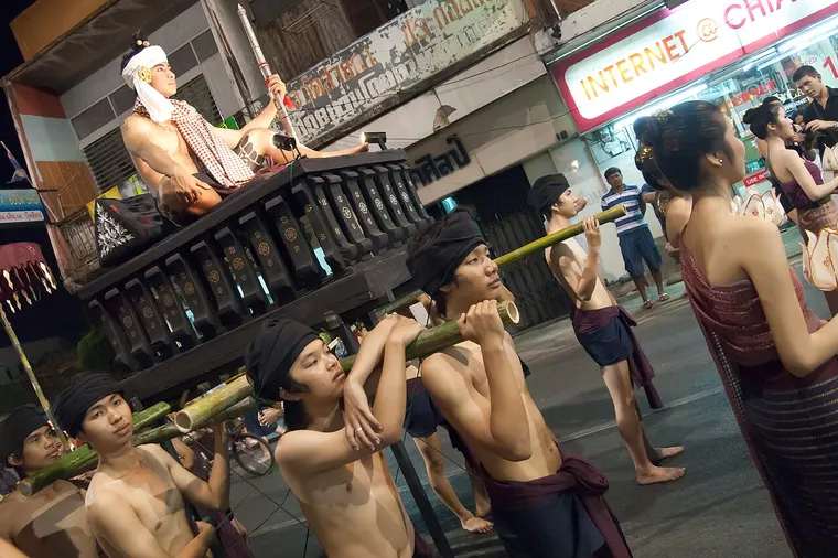 Młodzi mężczyźni w strojach niosą ozdobną platformę w paradzie festiwalu Loy Krathong w Chiang Mai