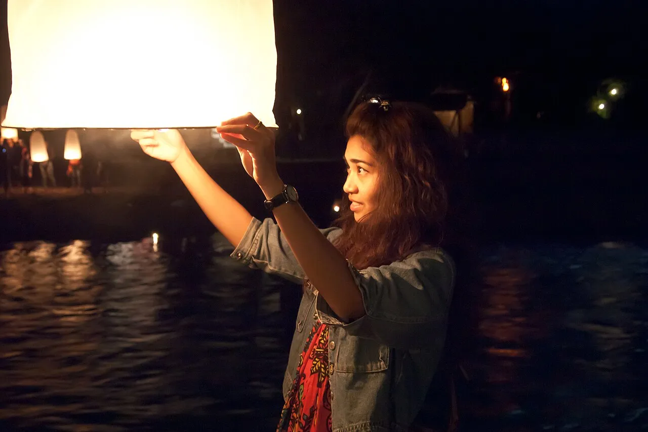 Kobieta unosi świecący lampion nad rzeką podczas festiwalu w Chiang Mai