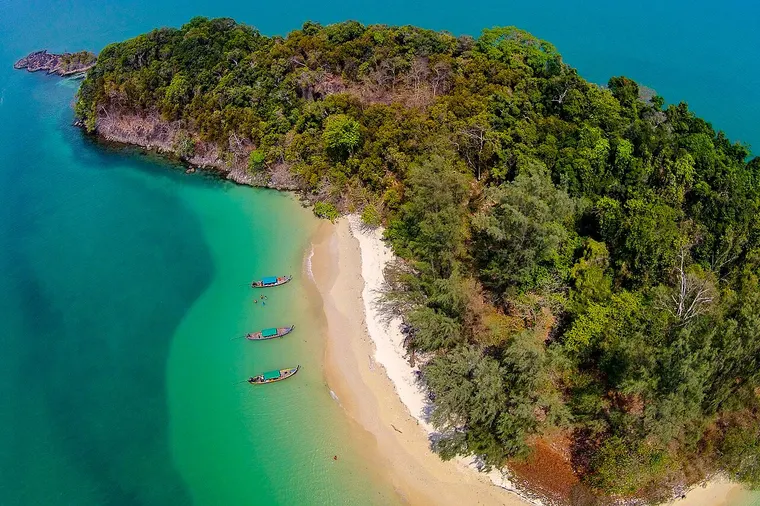 Zalesiona wyspa z plażą i łodziami w Morskim Parku Narodowym Laem Son