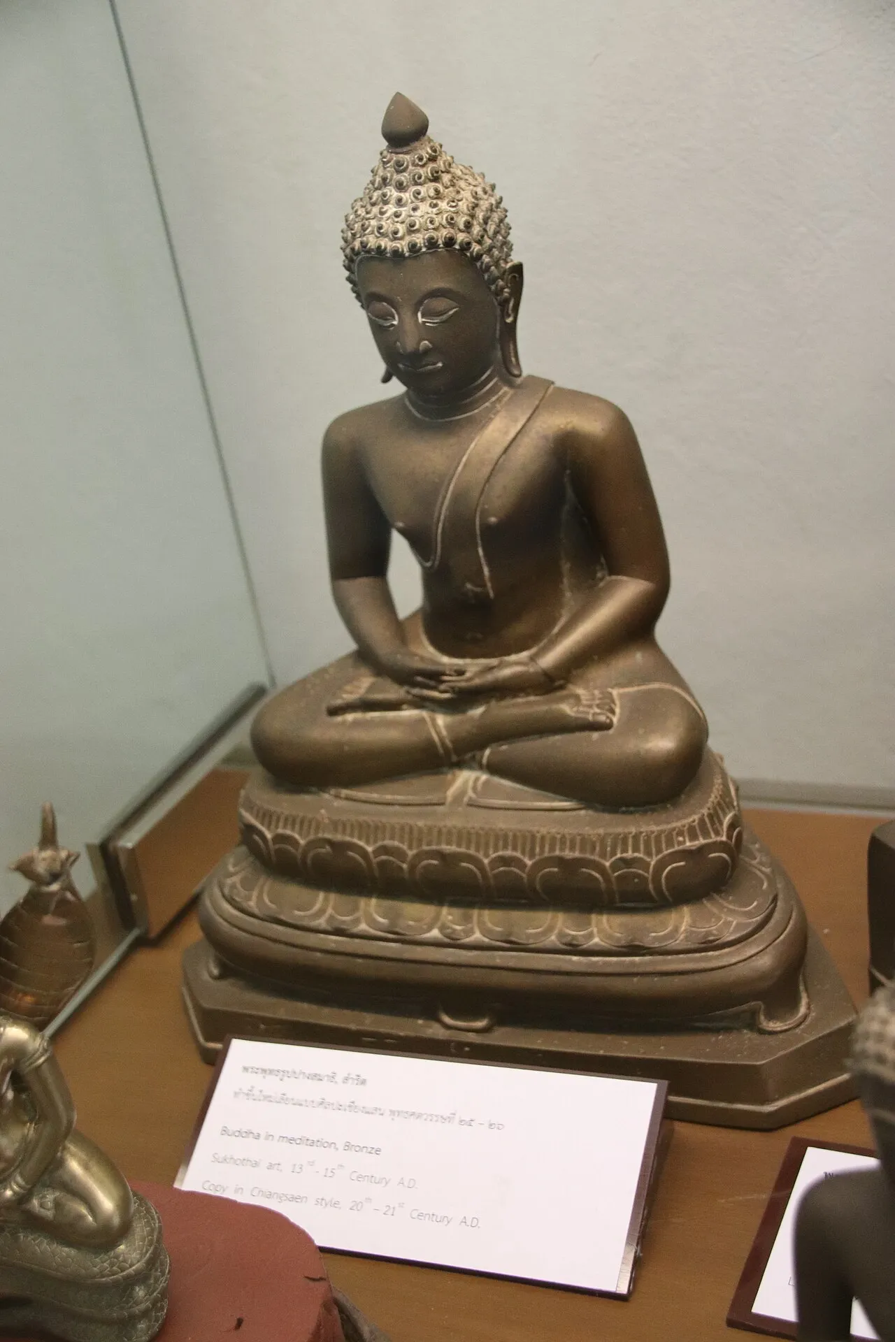 Brązowa figura medytującego Buddy w gablocie muzeum