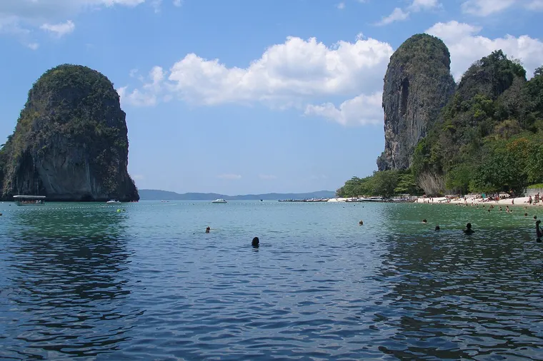 Słoneczna plaża Railay w prowincji Krabi z wapiennymi skałami i łodziami na turkusowej wodzie