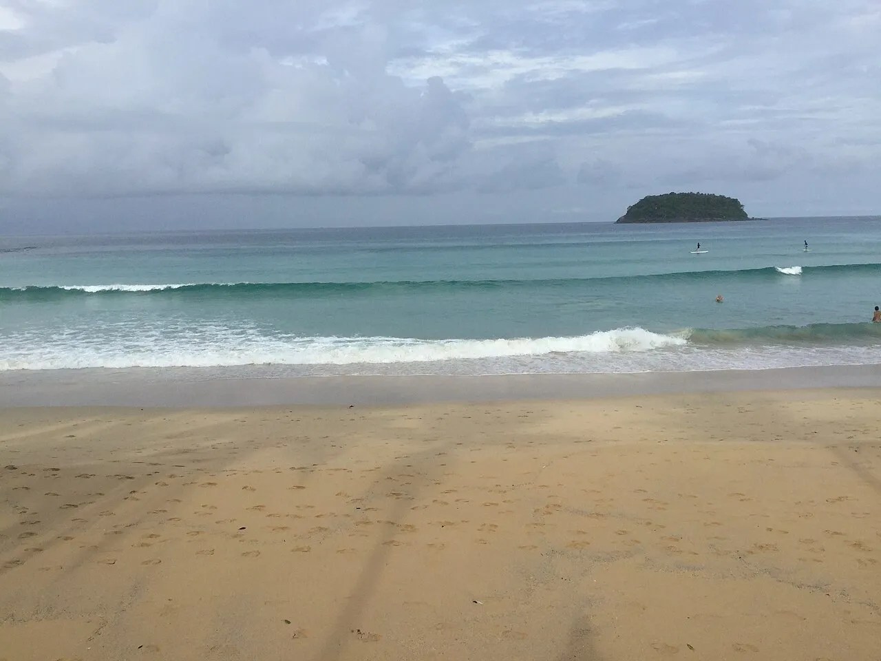 Szeroka, piaszczysta plaża Kata na Phuket z falami i małą wyspą Ko Pu na horyzoncie