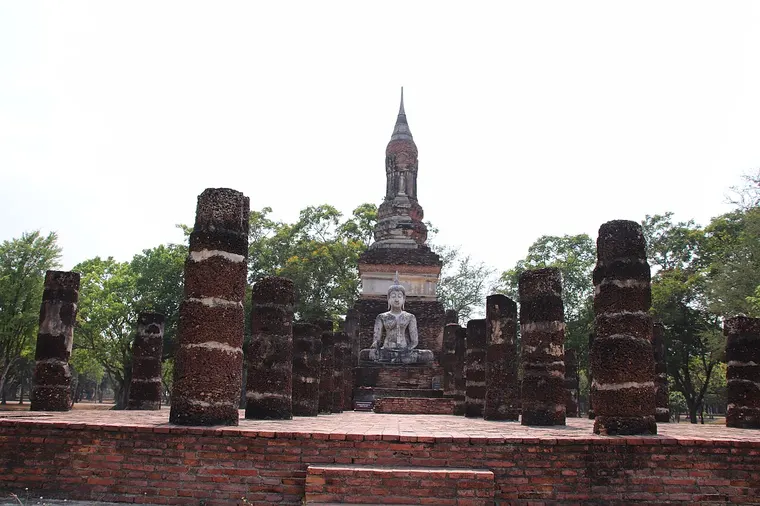 Ruiny świątyni w Parku Historycznym Sukhothai z posągiem Buddy między ceglanymi kolumnami