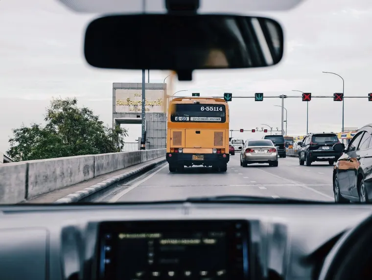 Widok zza kierownicy samochodu na ruch uliczny w Bangkoku, przed autem żółty autobus miejski