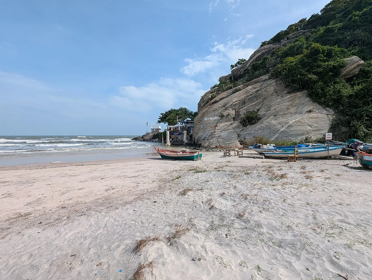 Piaszczysta plaża z łodziami rybackimi pod skalistym wzgórzem w Hua Hin