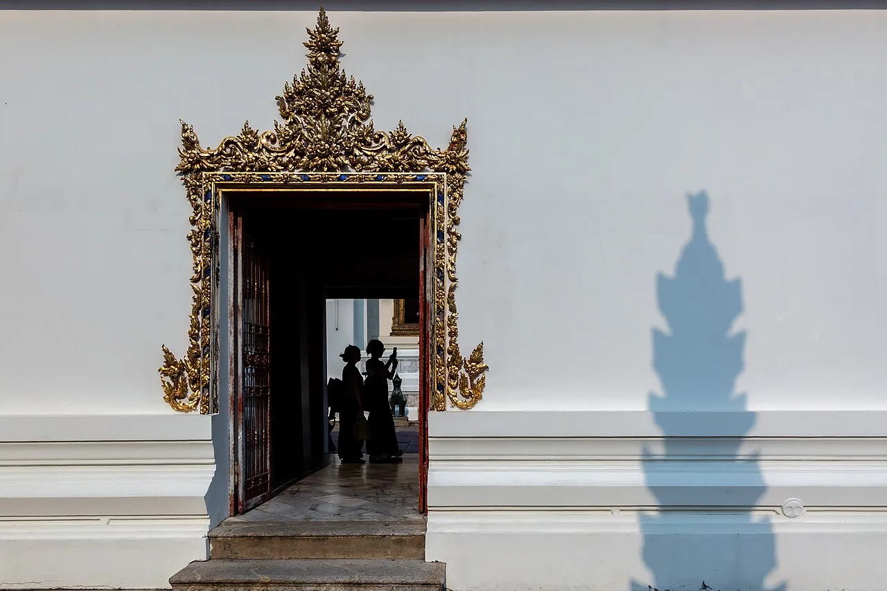 Zdobiony złoceniami portal w murze świątyni Wat Pho w Bangkoku i sylwetki zwiedzających