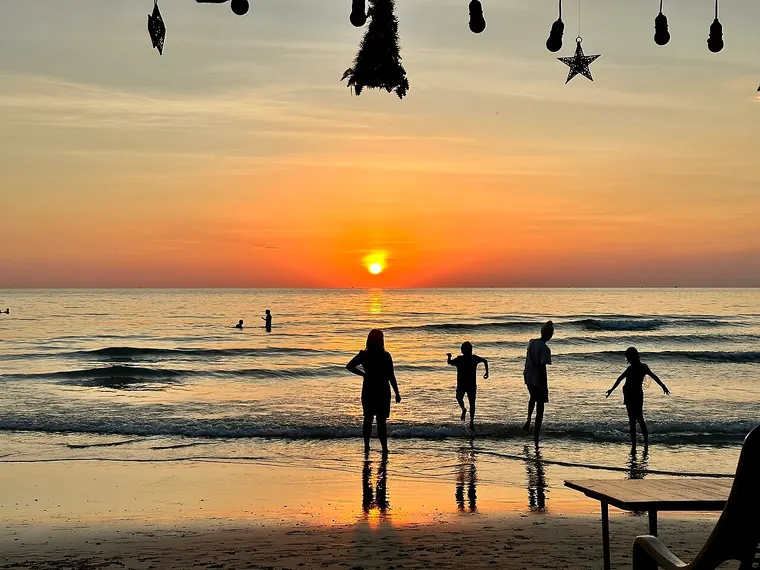 Sylwetki dzieci i dorosłej osoby brodzących w morzu na tle zachodu słońca na plaży na wyspie Ko Chang