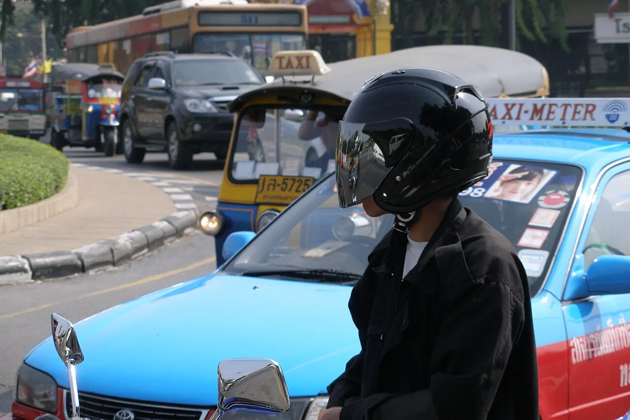Motocyklista w kasku między taksówkami i tuk-tukami w centrum Bangkoku